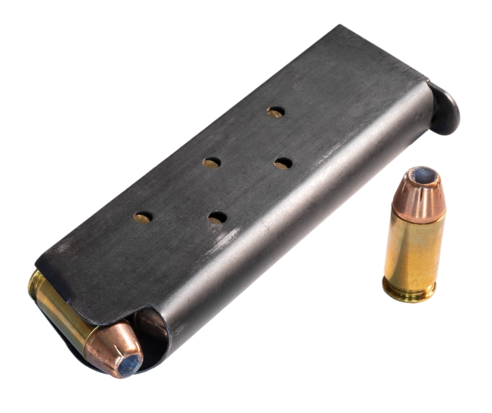 Metal magazine for a semi-auto 1911 pistol that is loaded with ammunition with one cartridge alone on the side isolated in a white background..