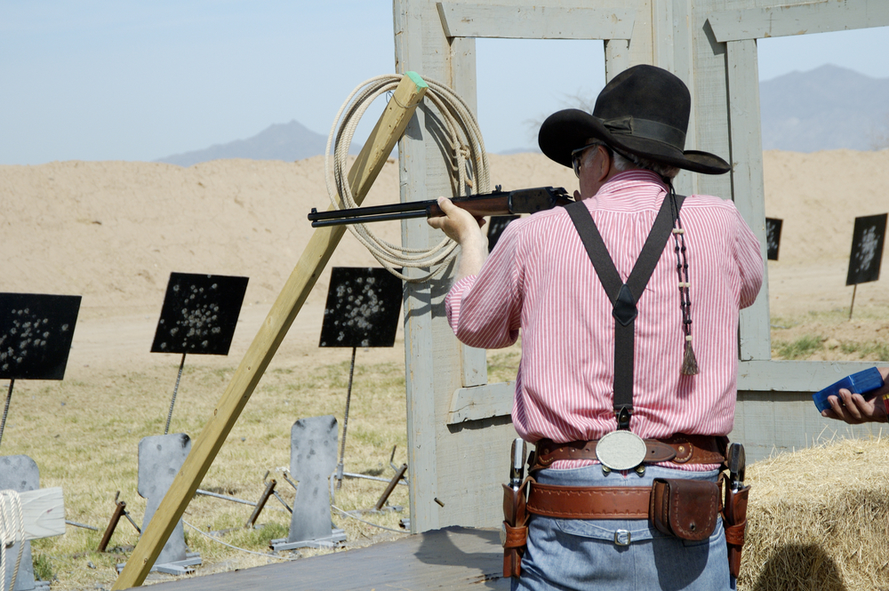Competitor shooting a lever action rifle in a cowboy shoot competition.