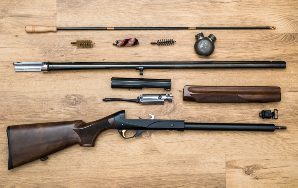 disassembled shotgun parts and cleaning kit on the wooden background